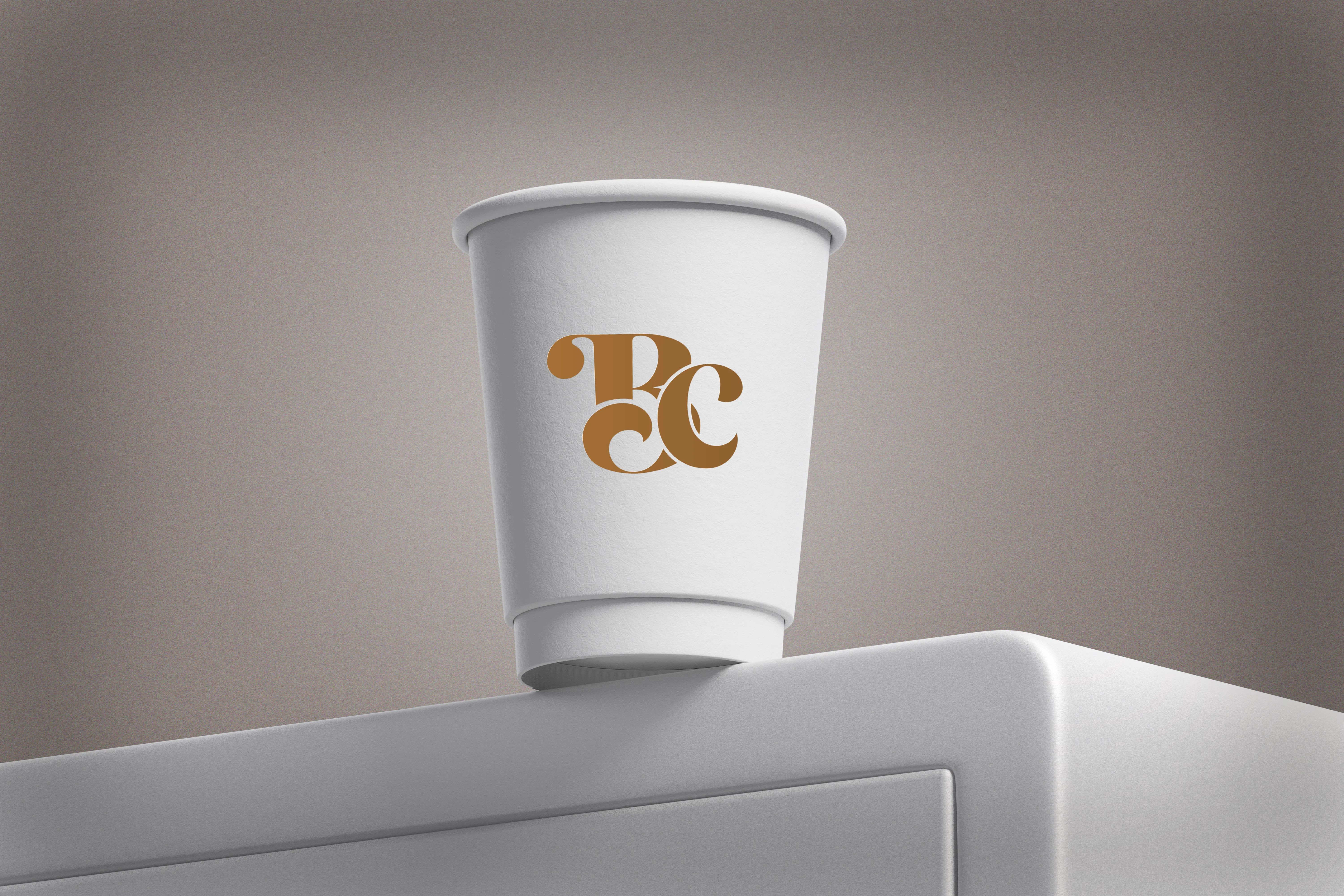 Vaso blanco de cartón sublimado con un logotipo dorado al frente, colocado sobre una superficie clara y fondo neutro.