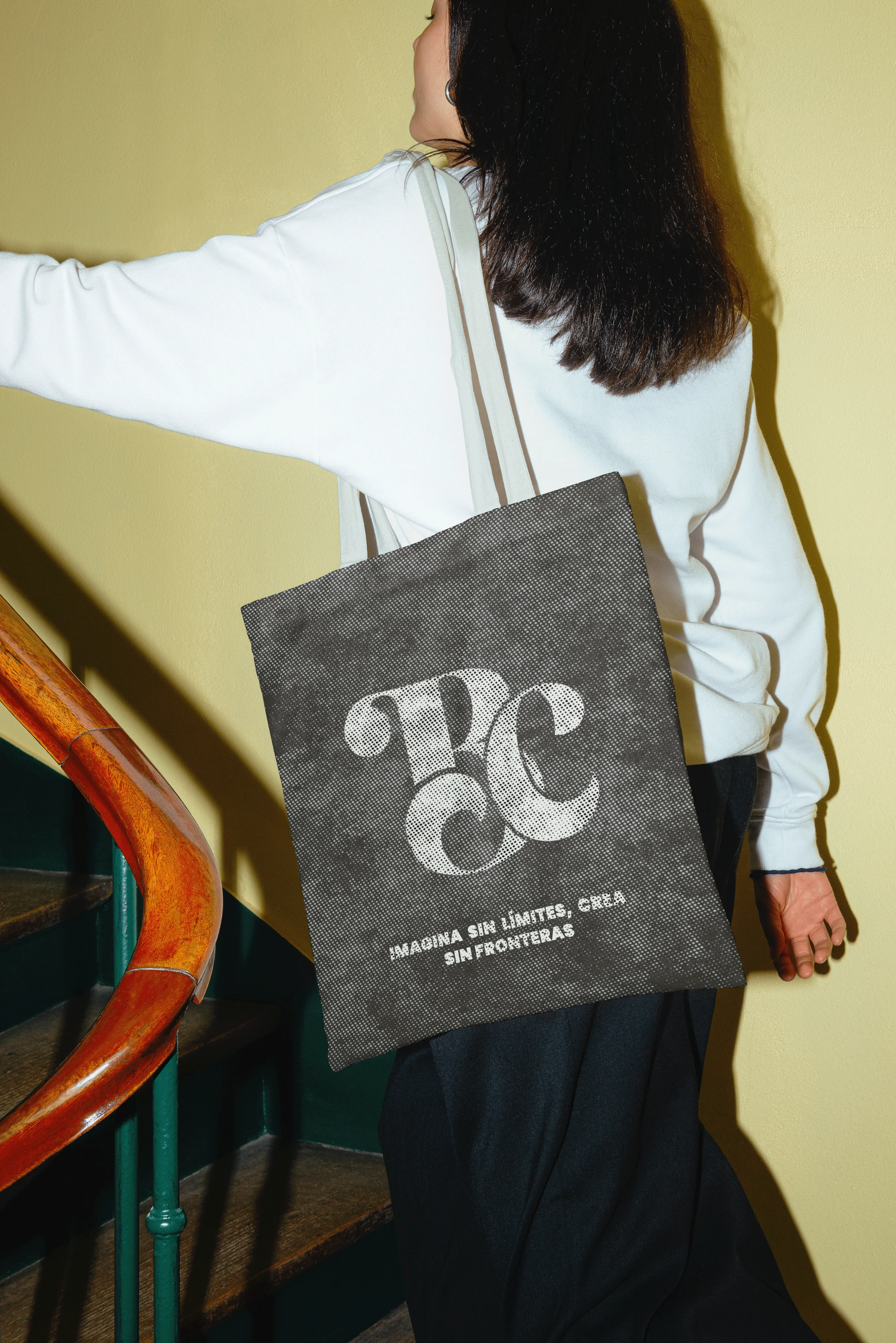 Mujer subiendo escalera con tote bag negra personalizada con logotipo y texto blanco.