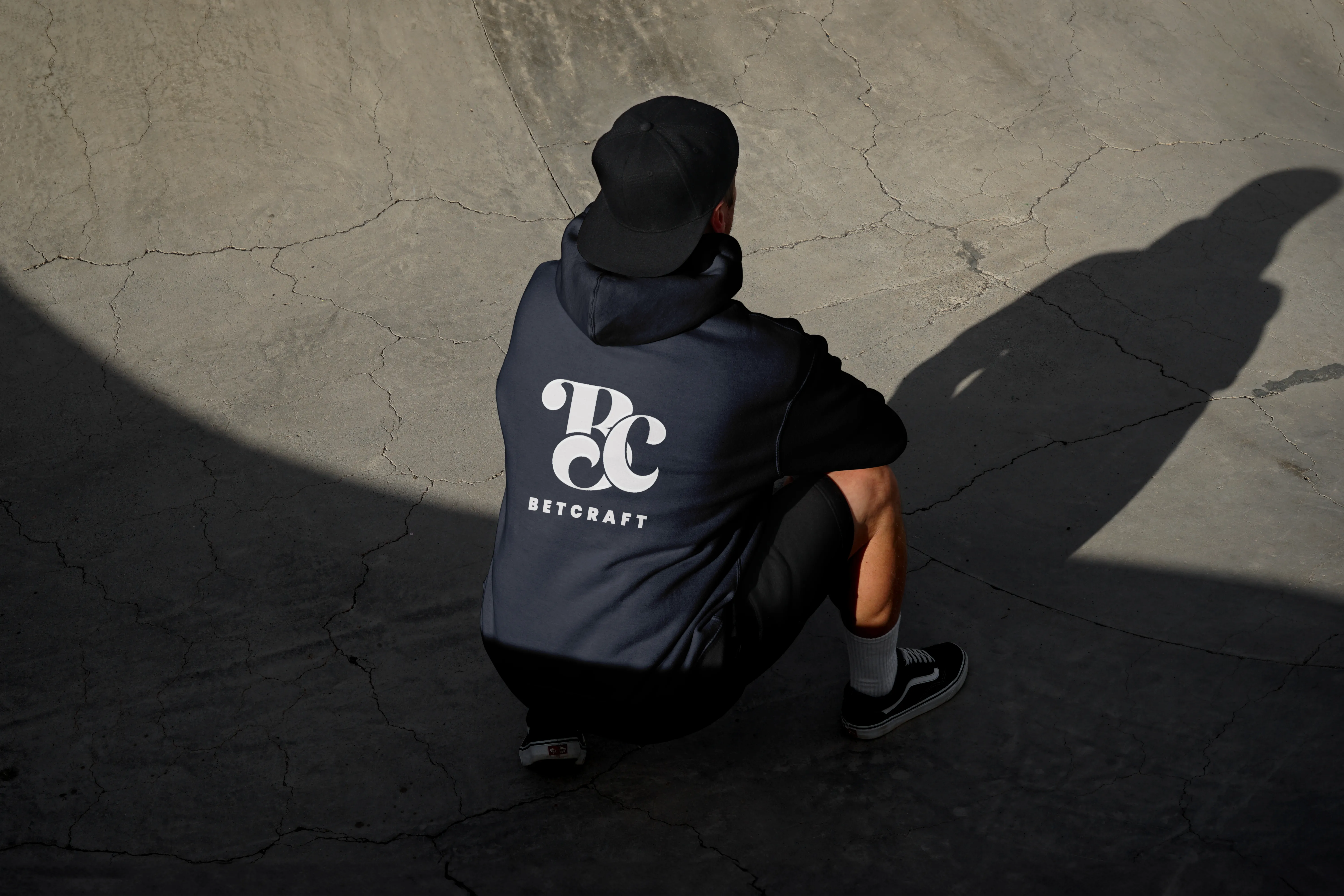 Chico de espaldas con gorra y sudadera negra con logo de Betcraft estampado.